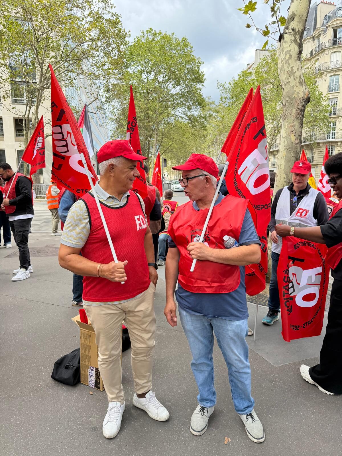 Deux agents en gilet rouge FO échangent, drapeaux au vent.