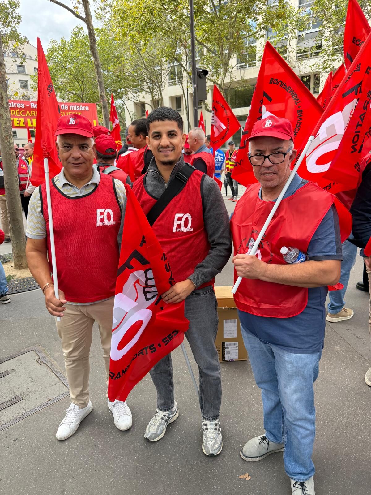 Trois agents FO, dont un jeune adhérent, sourient devant le cortège.